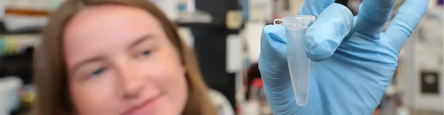 A Students holds a vial in a gloved hand